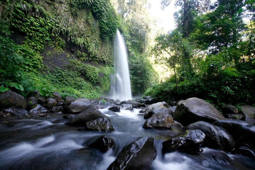 A beautiful waterfall cascades in West Nusa Tenggara, surrounded by lush greenery and rocks.