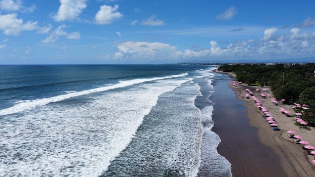 Breathtaking aerial view of Bali's beach with vibrant pink umbrellas and waves crashing on the shore.