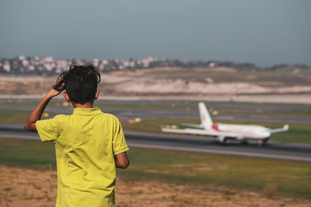 A young boy in a yellow shirt observing an airplane on the runway at an airport.