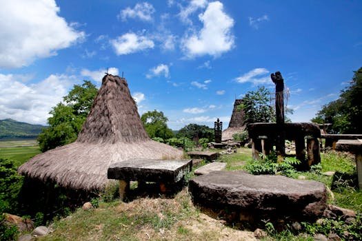 Scenic view of ancient Marapu structures and thatched roofs in Sumba, Indonesia under a bright blue sky.
